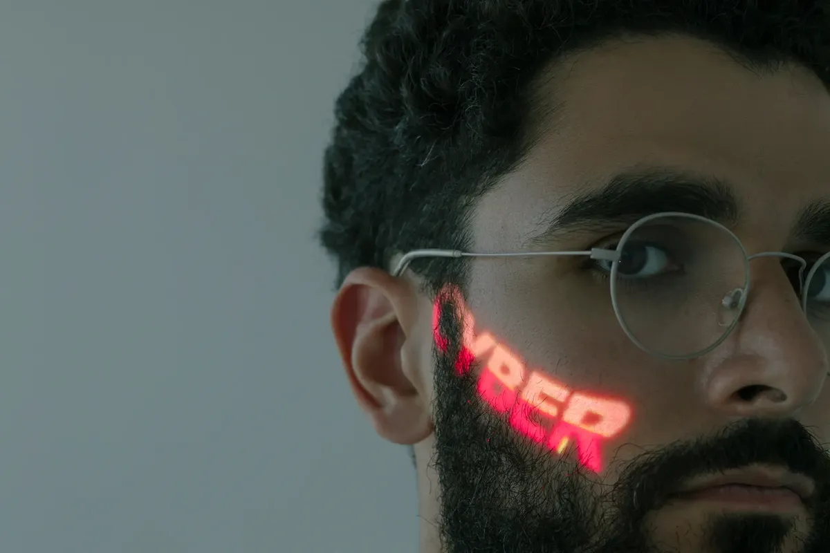 Close-up of a bearded man wearing eyeglasses with 'CYBER' text projected on his face.
